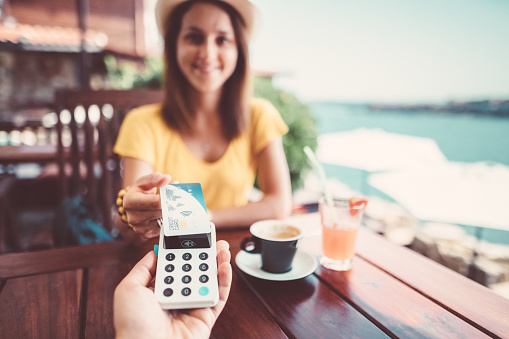 Smiling tourist woman sitting at cafe and paying with credit card for drinks