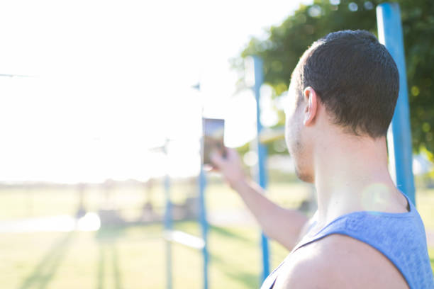 Young man snaps the sunrise, taking a picture on his mobile phone during early morning exercising routine in the park.