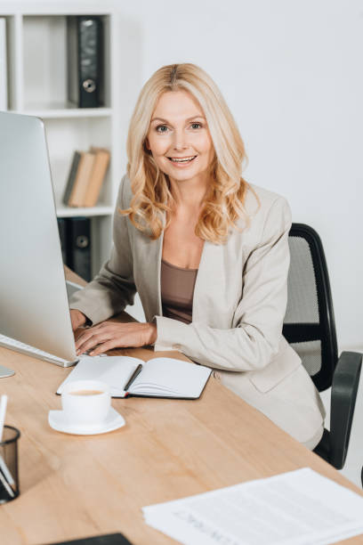 istock cheerful mature businesswoman using desktop computer and smiling at camera in office 1095911062