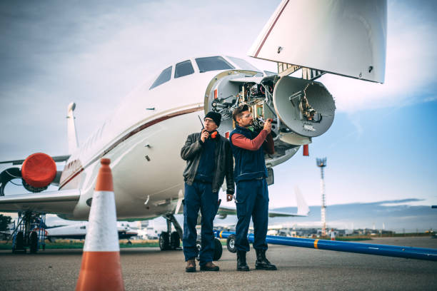 Two aircraft engineers working on a sensor array in the nose cone of an airplane parked outside on a tarmac