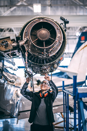 Senior female engineer doing some maintenance on an aircraft jet engine in a hangar.