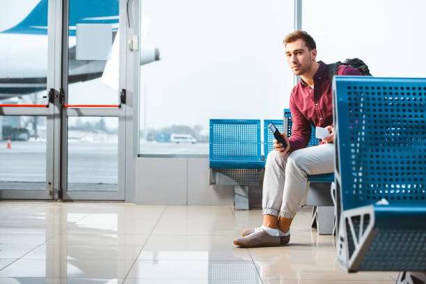 istock handsome man holding smartphone and passport while sitting in departure lounge 1095928632