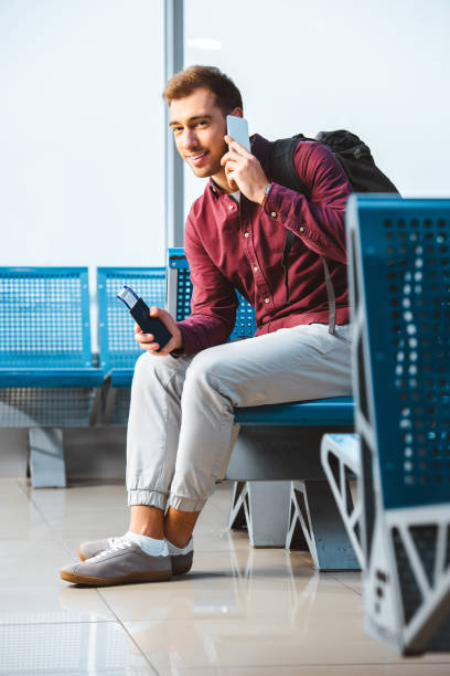 istock cheerful man talking on smartphone and smiling while sitting in waiting hall 1095928636