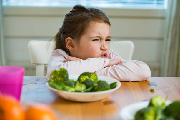 Cute girl eating spinach and broccoli at the table stock photo