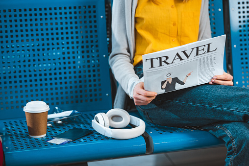 cropped view of woman reading newspaper near headphones in airport