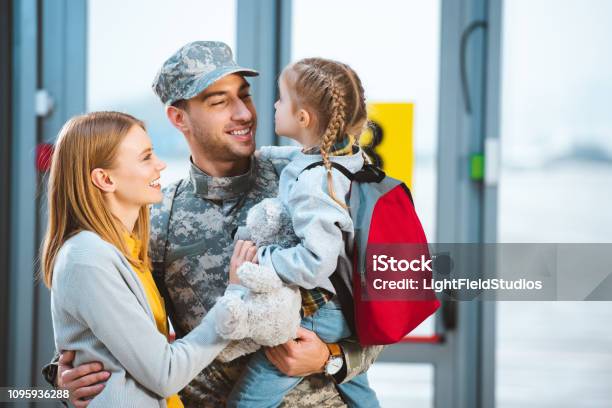 Foto de Pai Sorridente Em Uniforme Militar Segurando Na Filha De Braços Perto Da Esposa No Aeroporto e mais fotos de stock de Tropas