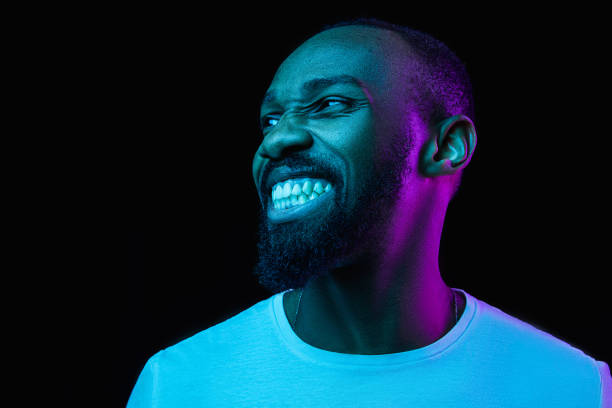 The neon portrait of a young smiling african man The retro wave or synth wave portrait of a young happy smiling african man at studio. High Fashion male model in colorful bright neon lights posing on black background. Art design concept macho photos stock pictures, royalty-free photos & images