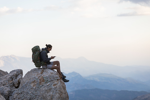 Man sitting at the edge of a cliff using phone.