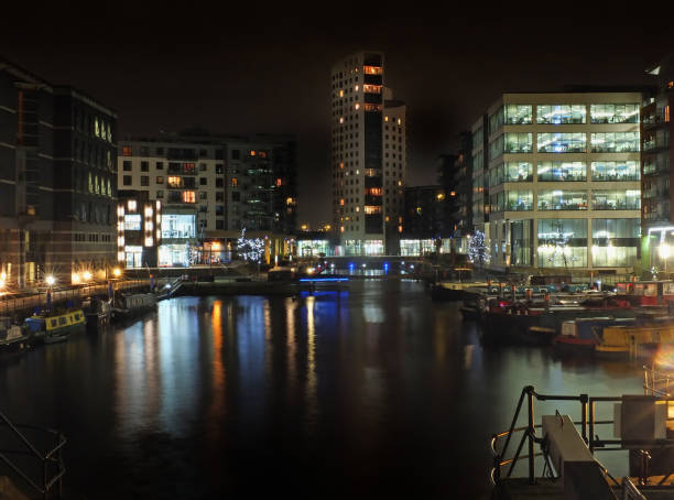 clarence dock in leeds at night with brightly illuminated buildings reflected in the water and boats moored along the sides - leeds england yorkshire canal museum imagens e fotografias de stock