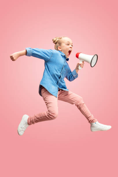красивый маленький ребенок подросток девушка прыгает с мегафоном изолированы на розовом фоне - people moving audio стоковые фото и изображения