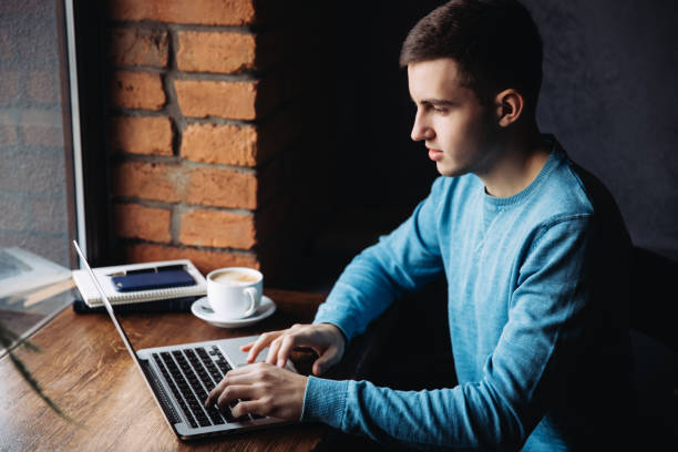 istock Young programmer with laptop in cafe sits opposite the window 1095976836