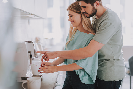 Waist up photo of happy woman and man making coffee with machine at home
