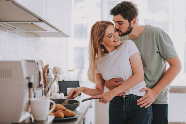 Happy lovers cooking food and showing their feelings Young bearded man gently kissing his charming girlfriend while she stirring something in pan boyfriend stock pictures, royalty-free photos & images
