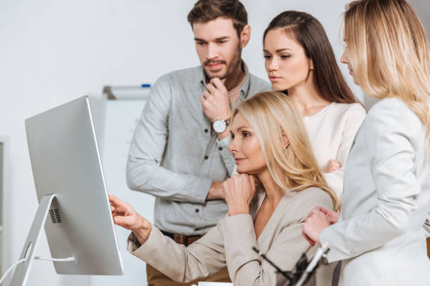 istock mature business mentor pointing at desktop computer and working with young colleagues in office 1095985312