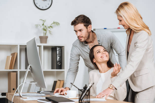 istock smiling mature business mentor looking at young colleagues working with desktop computer in office 1095985372