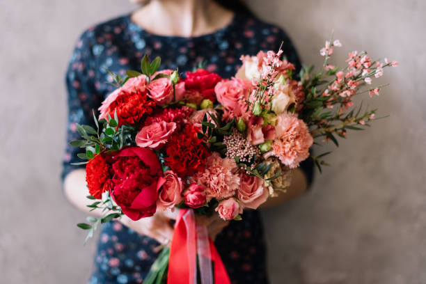 Very nice young woman holding beautiful blossoming flower bouquet of fresh roses, carnations, in passionate red colors on the grey background stock photo