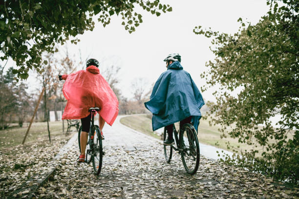 Rear View Of Couple In Raincoats Riding A Bikes In The Park stock photo
