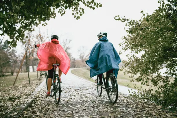 Rear View Of Couple In Raincoats Riding A Bikes In The Park