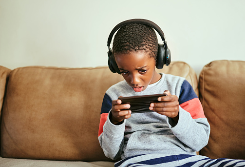 Shot of an adorable little boy using a smartphone and headphones on the sofa