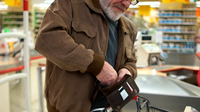 Close portrait of an elderly man with a purse in his hands in the supermarket. Pensioner smiles