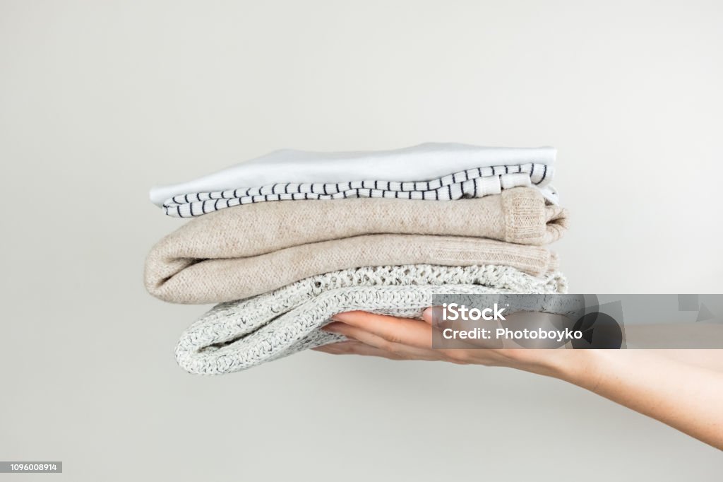 Heap of clothes in female hands Neatly stacked simple clothing at white background Clothing Stock Photo
