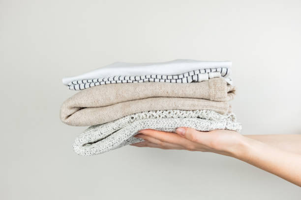 Heap of clothes in female hands Neatly stacked simple clothing at white background clothing donation stock pictures, royalty-free photos & images
