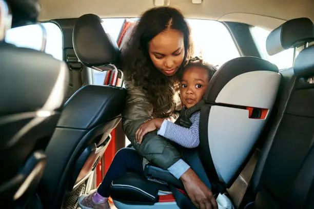 Shot of an adorable little girl being secured in her car seat by her mother