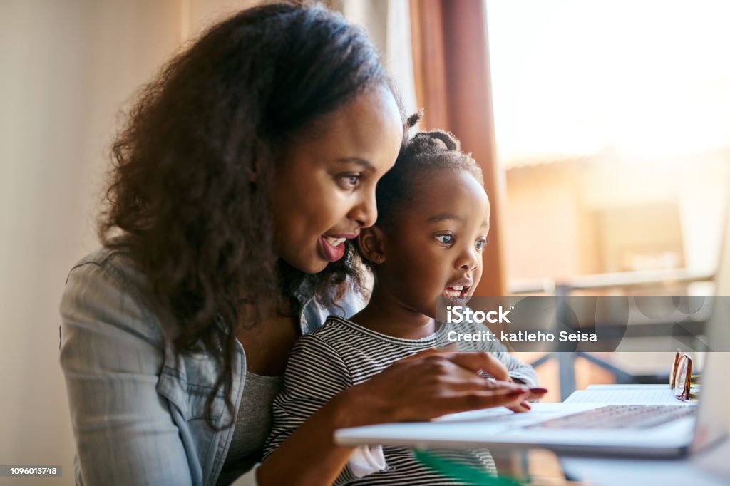 The internet is just what a curious mind needs Shot of an adorable little girl using a laptop with her mother at home Child Stock Photo