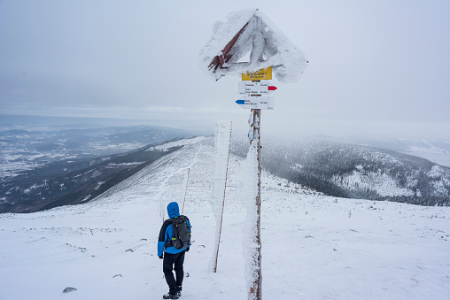 A man on a mountain trail next to a touristic indicator, all covered in snow