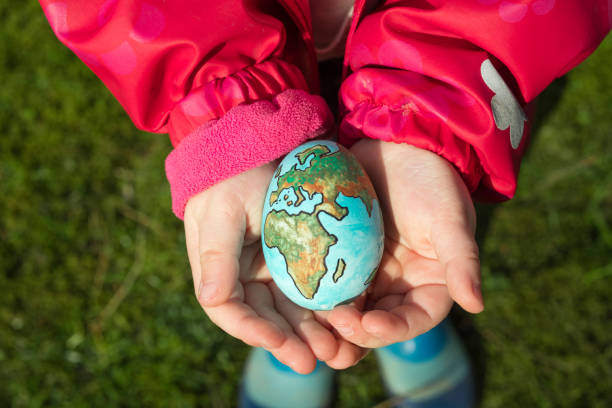 criança segurando um ovo com o planeta terra pintado em um dia ensolarado ao ar livre - child art paint humor - fotografias e filmes do acervo