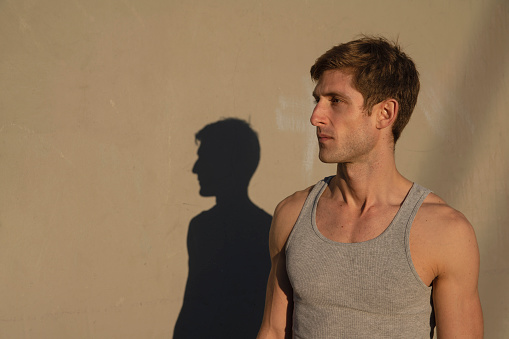 Portrait of the athletic man against the wall, with the shadow.