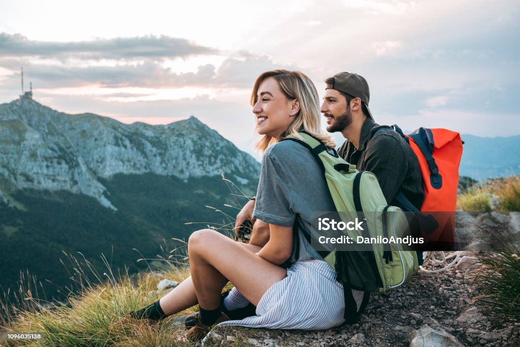 beautiful young couple relaxing after hiking and taking a break young couple of hikers enjoying the beautiful nature from high above Travel Stock Photo