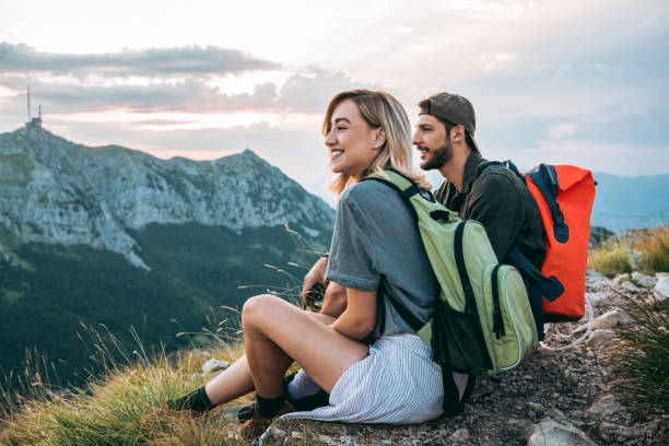 beautiful young couple relaxing after hiking and taking a break young couple of hikers enjoying the beautiful nature from high above backpacker stock pictures, royalty-free photos & images