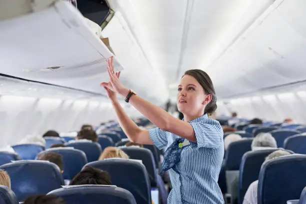 Shot of a young air hostess closing the overhead compartment on an airplane