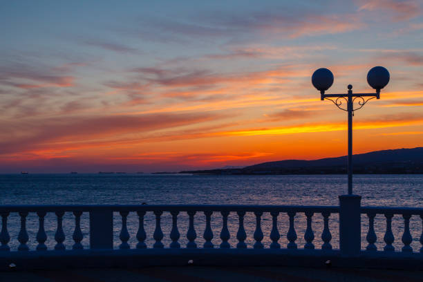 Sunset in Gelendzhik. The sun shines through the balustrade. Dramatic sunset in Gelendzhik. In the foreground promenade with balustrade and lights. On the back silhouettes of mountains in the evening twilight baluster stock pictures, royalty-free photos & images