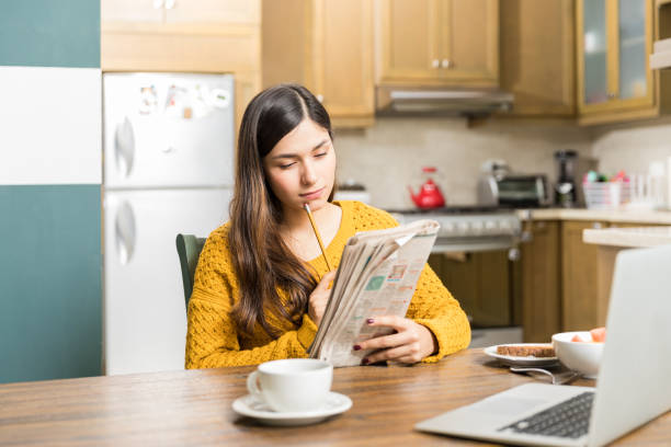 Woman Analyzing Newspaper Game Carefully Young woman thinking while solving crossword puzzle at table during breakfast time crossword stock pictures, royalty-free photos & images