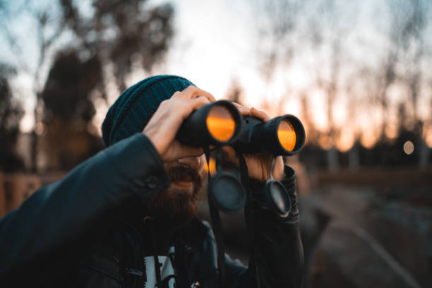 hombre barbudo con prismáticos mirando hacia el mar al atardecer - discovery binoculars boy scout searching fotografías e imágenes de stock