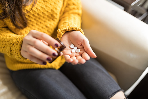 Midsection of woman in casuals pouring pills at home