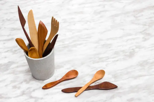 Handcrafted wooden utensils in a concrete cup, on marble background with copy space.