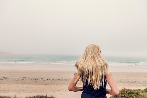 Woman with long blonde hair stood above Fistral Beach, Newquay, Cornwall looking at the view on an Autumn afternoon.