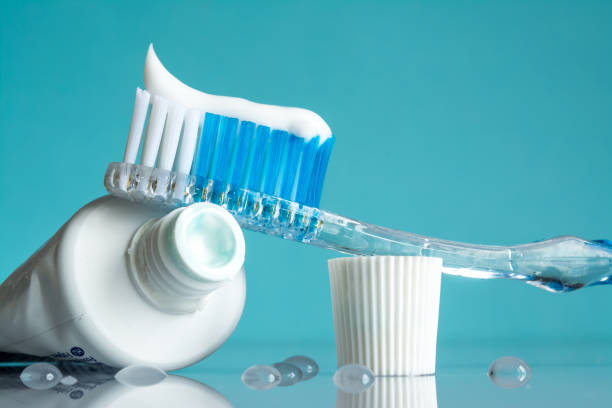 New toothbrush with toothpaste close-up in the bathroom on a mirror table with water drops on a blue background in the sunlight stock photo