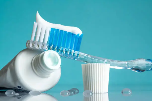 Photo of New toothbrush with toothpaste close-up in the bathroom on a mirror table with water drops on a blue background in the sunlight