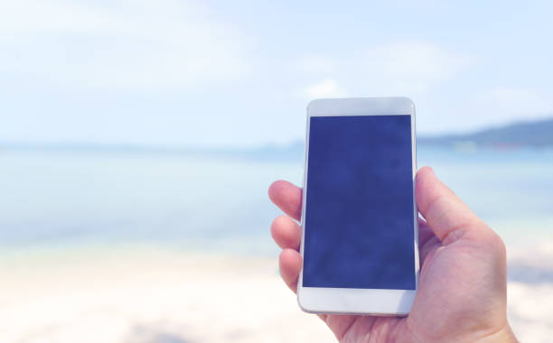 istock phone in hand on the beach background. mockup image 1096109442