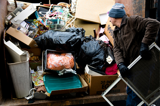 Workman loading junk in dumpster