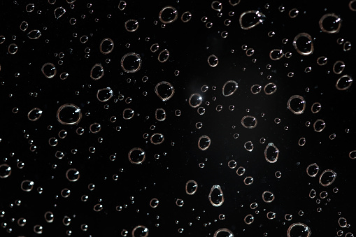 Detail photo - rain water drops behind glass look like bubbles in black liquid. Abstract wet background.