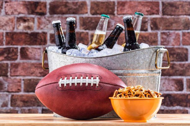 an american football with a tub of assorted ice cold beer bottles and a bowl of pretzels - american football football food snack imagens e fotografias de stock