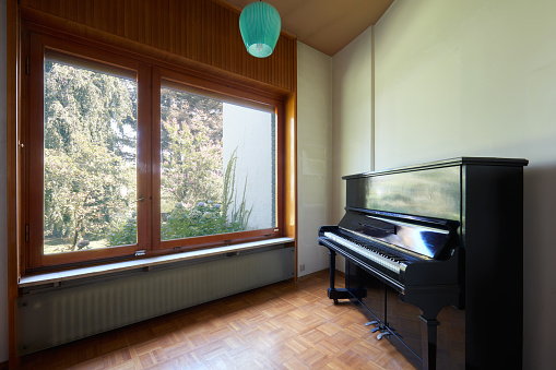 Room with piano and large window, apartment interior in old house with garden