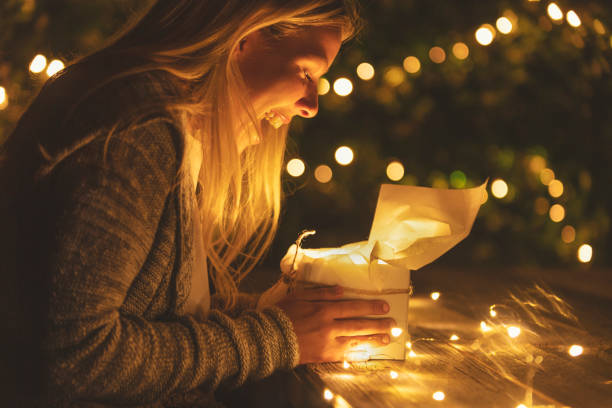 Woman opening a gift box with a gift inside. Her mouth is open in surprise.