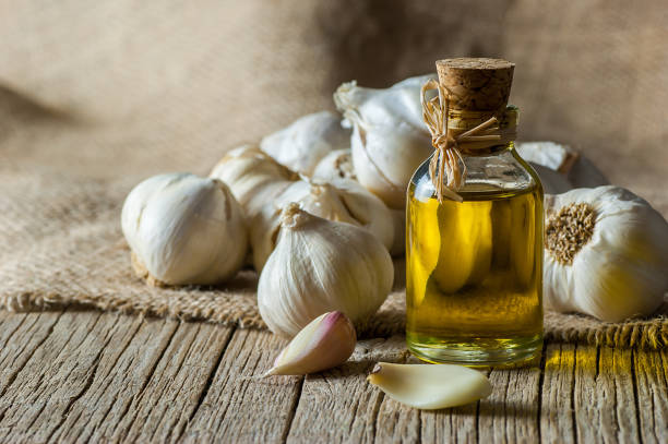 Ripe and raw garlic and garlic oil in glass of bottle on wooden table with burlap sack, alternative medicine, organic cleaner. Garlics background stock photo