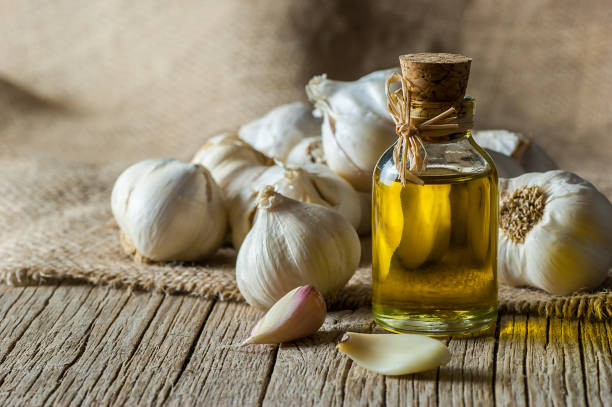 ripe and raw garlic and garlic oil in glass of bottle on wooden table with burlap sack, alternative medicine, organic cleaner. garlics background - garlic freshness isolated vegetarian food imagens e fotografias de stock